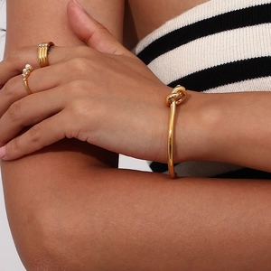 Gold knotted cuff bracelet with pearl and pavé diamond rings on a female model