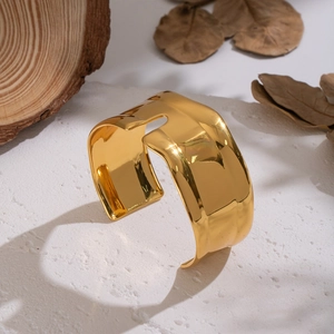 Golden wide geometric open bangle on a white stone surface with natural autumn decor