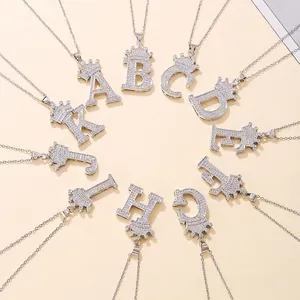 Silver crown letter necklaces A-K with cubic zirconia pavé on a warm beige background