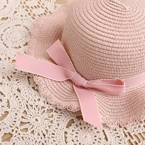 Gros plan d'un chapeau de paille rose avec bords dentelés et un joli nœud pour fille
