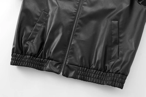 Close-up of black faux leather bomber jacket featuring an elastic hem and silver zipper