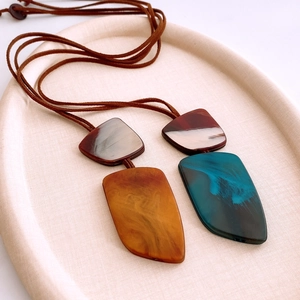 Detail of irregular marble textured resin geometric pendants on brown suede cords