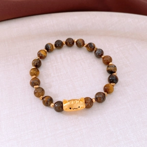 Détail d'un bracelet en œil de tigre avec breloque chat dorée sur tissu texturé