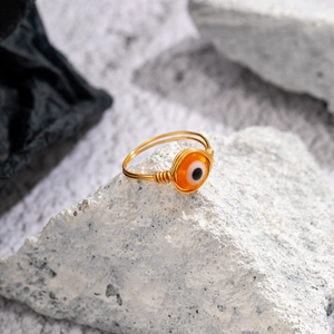 Macro detail of handmade gold wire wrapped orange evil eye ring on a textured stone