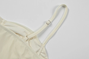 Detailed close-up of adjustable metal buckles and spaghetti straps on cream dress