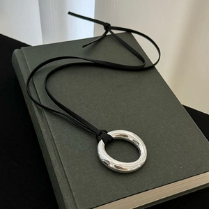 Close-up of a high-polished silver round pendant on a black leather cord necklace
