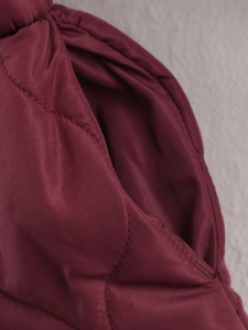 Close-up of the burgundy quilted jacket showing high-quality pocket stitching and fabric