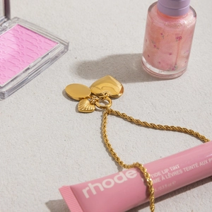 Collier chaîne dorée avec pendentifs cœur et coquillage, présenté avec des accessoires beauté