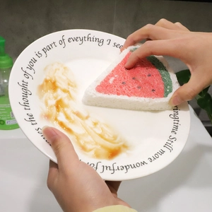 Watermelon shaped wood pulp cellulose kitchen sponge cleaning a stained ceramic plate