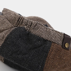 Close-up of herringbone tweed octagonal cap with brown leather strap and metal buckle