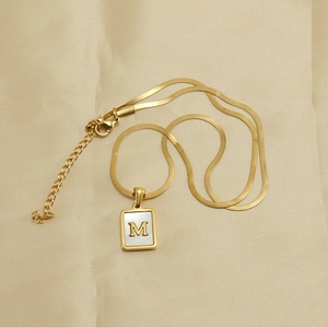 Detail of gold snake chain necklace with square shell pendant featuring initial letter M
