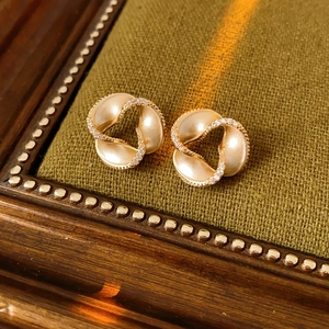 Close-up of elegant gold spiral earrings with pavé diamonds on green textured fabric