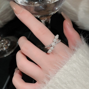 Detail of elegant cross design ring with white pearls and zircon accents on finger