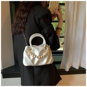 Detail of white pleated cloud bag featuring marble bead handle and silver chain strap