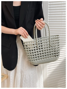 Close-up of greyish green woven jelly basket bag held by a model in a casual summer outfit