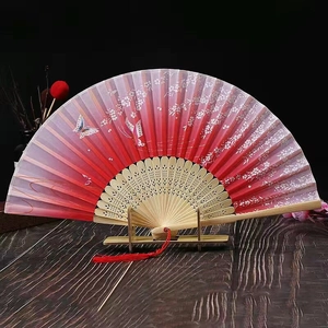 Close-up of a pink gradient cherry blossom fan with bamboo ribs and red tassel on a stand