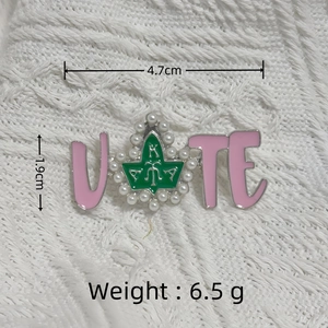 Detail view of pink and silver VOTE brooch with green leaf and small pearl accents