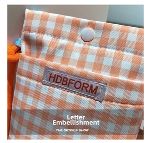 Detail of orange checkered canvas mini bag featuring HDBFORM label and snap button