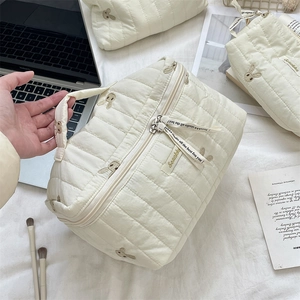 Detailed close-up of quilted cream makeup bag featuring cute rabbit embroidery and side handle