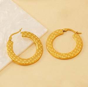 Detail of gold stainless steel hoop earrings featuring textured star relief patterns