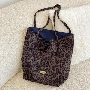Detailed view of leopard print tote bag with gold metal logo plaque on a soft sofa
