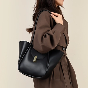 Détail du sac cabas en cuir noir mat avec boucle dorée porté par un mannequin en trench