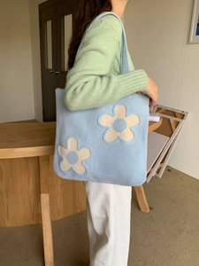 Close-up of light blue knitted tote bag with large white floral applique detail