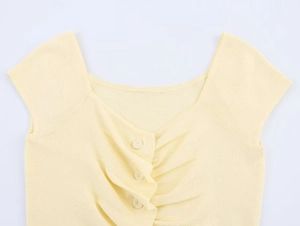 Detail of light yellow knit top featuring small buttons and pleated chest design