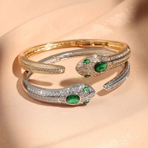 Nahaufnahme von Gold- und Silberschlangenarmbändern mit grünen Edelsteinen und Kristallen