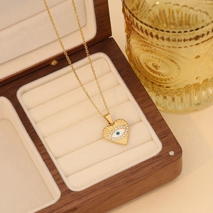 Close-up of gold heart necklace with blue evil eye pendant in a wooden jewelry box