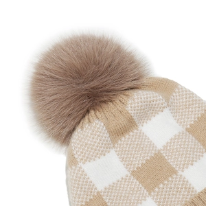 Detail view of winter knit beanie showing beige plaid texture and fluffy brown pompom