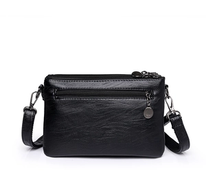 Detalle de bolso bandolera de cuero granulado negro con múltiples cremalleras y herrajes