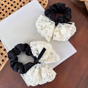 Detail of white floral lace bow scrunchie with intricate embroidery on black silk fabric