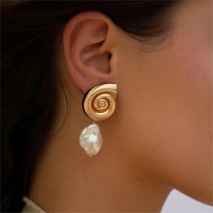 Golden spiral conch earring with irregular pearl drop shown on a female model