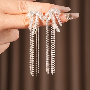 Detail view of silver bowknot tassel earrings with cubic zirconia held by a hand