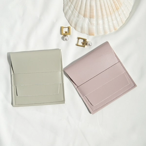 Minimalist grey and pink PU leather jewelry pouches on white textured fabric background
