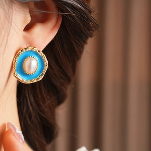 Detail of vintage gold earrings with sky blue enamel and center white pearl on a model