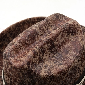 Close-up of distressed dark brown faux leather texture and white braided rope on cowboy hat