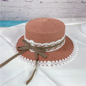 Close-up of orange straw hat with white lace trim and plaid ribbon bow detail
