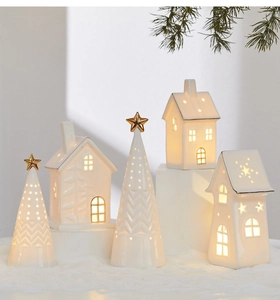 Close-up of glowing white ceramic Christmas trees and cutout houses with warm LED lighting