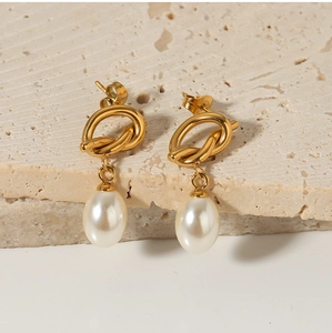 Detail of gold knot earrings with white teardrop pearls on a textured stone background