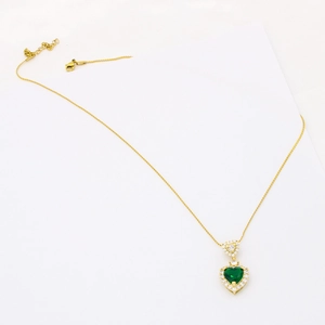 Close-up of golden heart pendant with emerald green stone and clear zircon setting