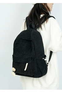Detail eines schwarzen Cord-Rucksacks mit strukturierter Seitentasche und Bärenanhänger