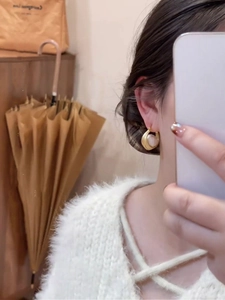 Gros plan d'une créole en perles plaquée or 16 carats portée dans un style français minimal