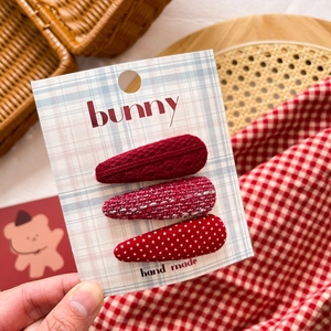 Detailed set of red fabric bow hair clips for girls displayed on a checkered card