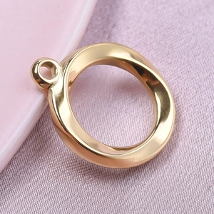 Macro detail of a golden twisted round pendant with a hanging loop on pink fabric