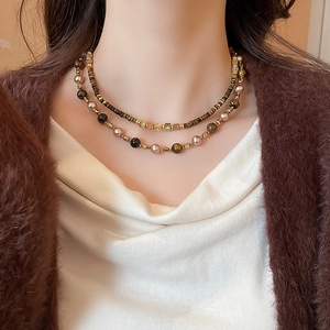 Detail of a double-layered pearl necklace with tiger eye stones on a brown cardigan
