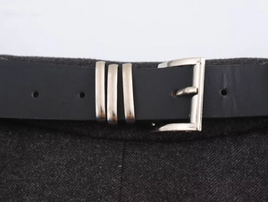 Detail of black leather belt with silver buckles on a dark grey wool skirt fabric