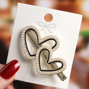 Detailed view of elegant double heart hair clip with white pearls and gold metal base