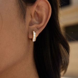 Gros plan détaillé d'une boucle d'oreille créole dorée avec diamants baguette sur l'oreille